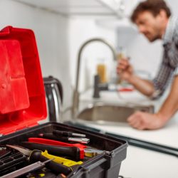 Selective focus of instrument in toolbox and plumber working in kitchen